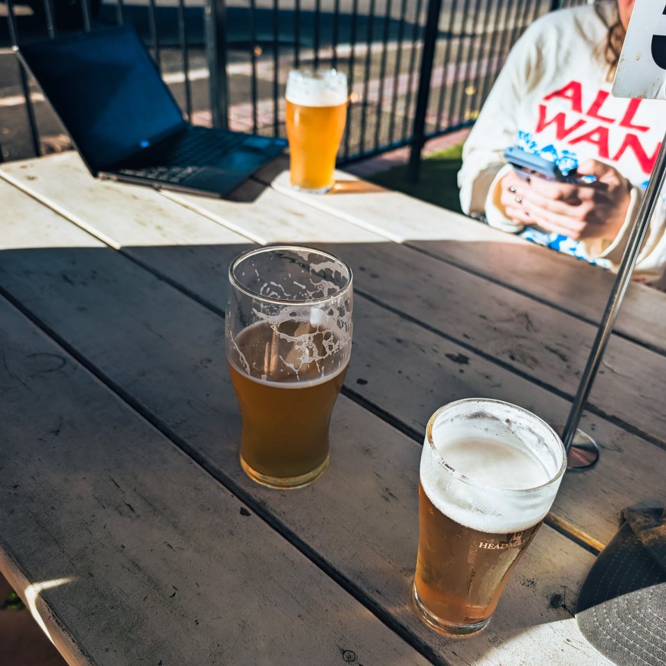 Two glasses of beer on a wooden table outdoors.