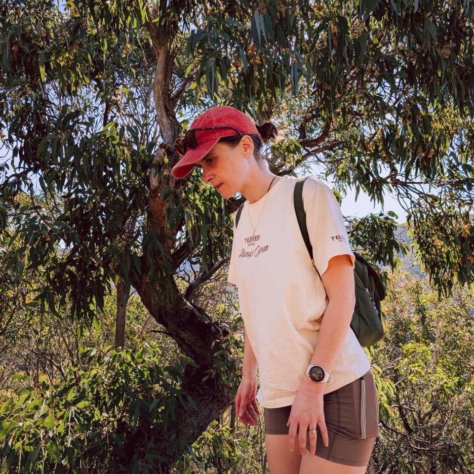 Person wearing a red hat standing in a dense eucalypt forest.
