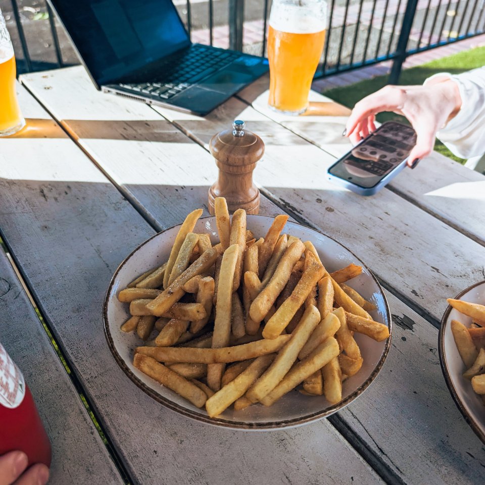 Golden french fries and beer on a wooden table outdoors.