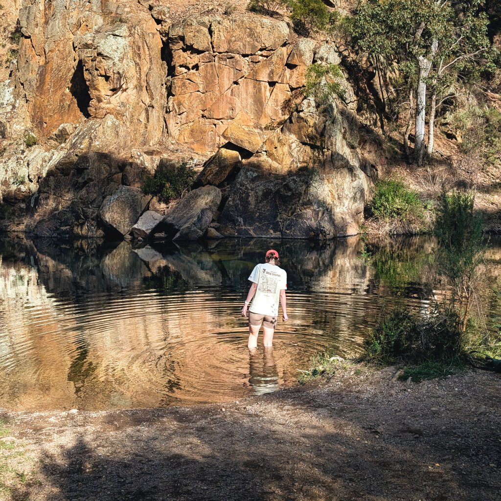 Person standing in shallow water near a rocky riverbank in a gorge setting.