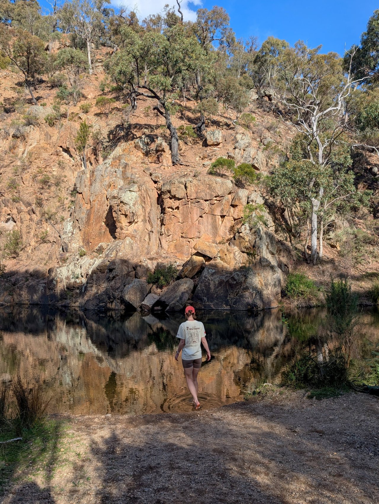 Person standing near a river in a dry, rocky gorge area with eucalypt trees.