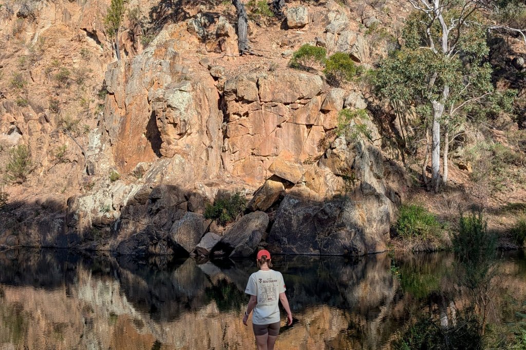 Person standing near a river in a dry, rocky gorge area with eucalypt trees.