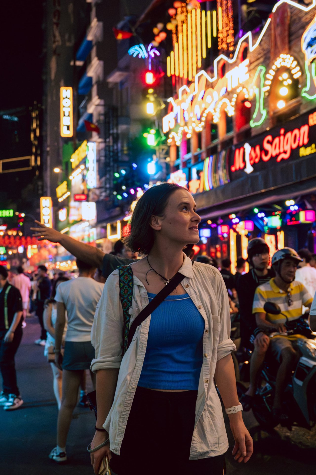 Woman walking on a vibrant street filled with colorful neon lights in Ho Chi Minh City.