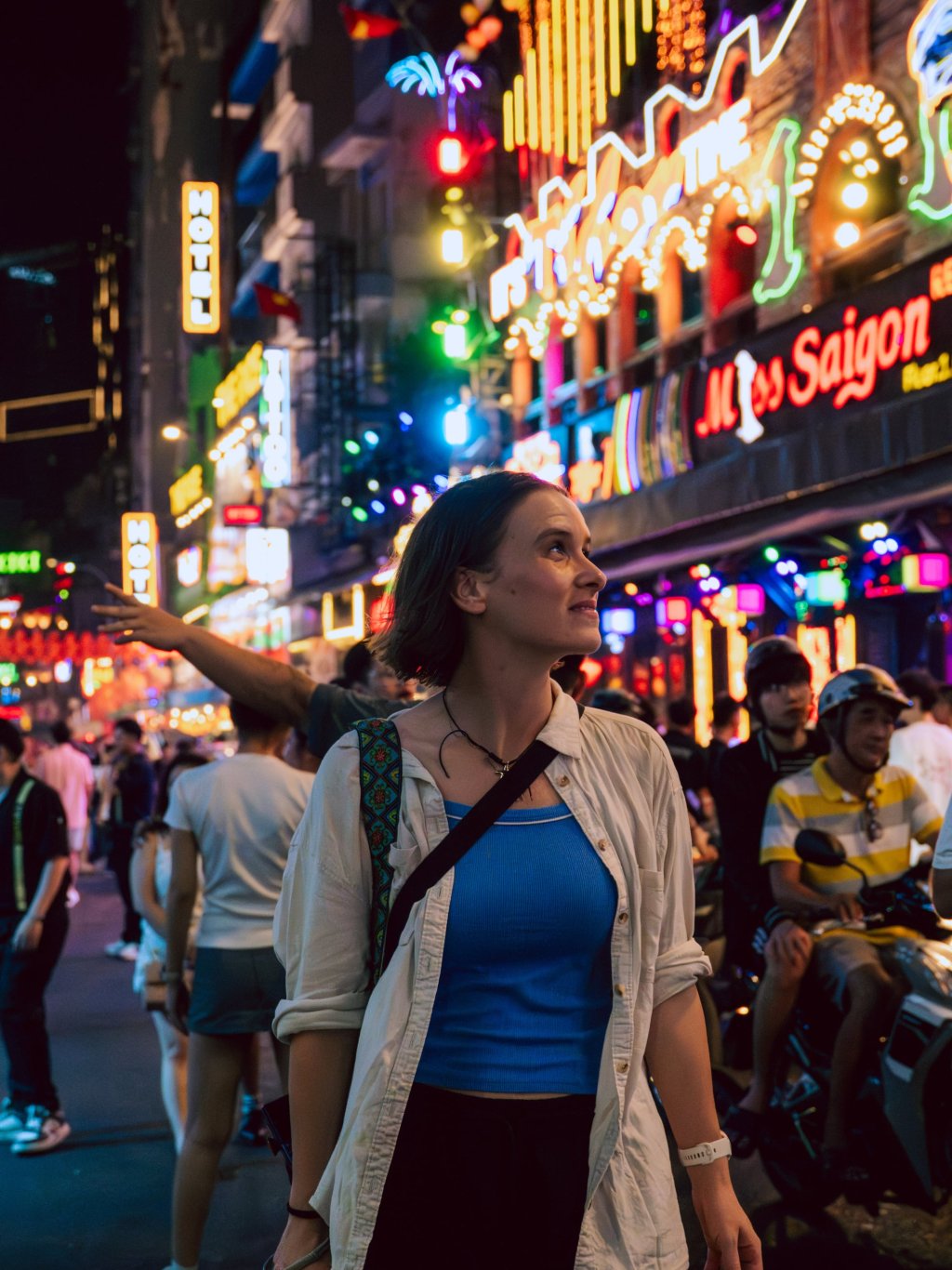 Woman walking on a vibrant street filled with colorful neon lights in Ho Chi Minh City.