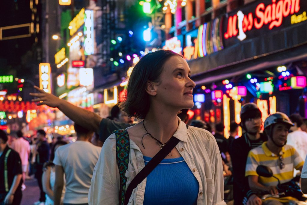 Woman walking on a vibrant street filled with colorful neon lights in Ho Chi Minh City.
