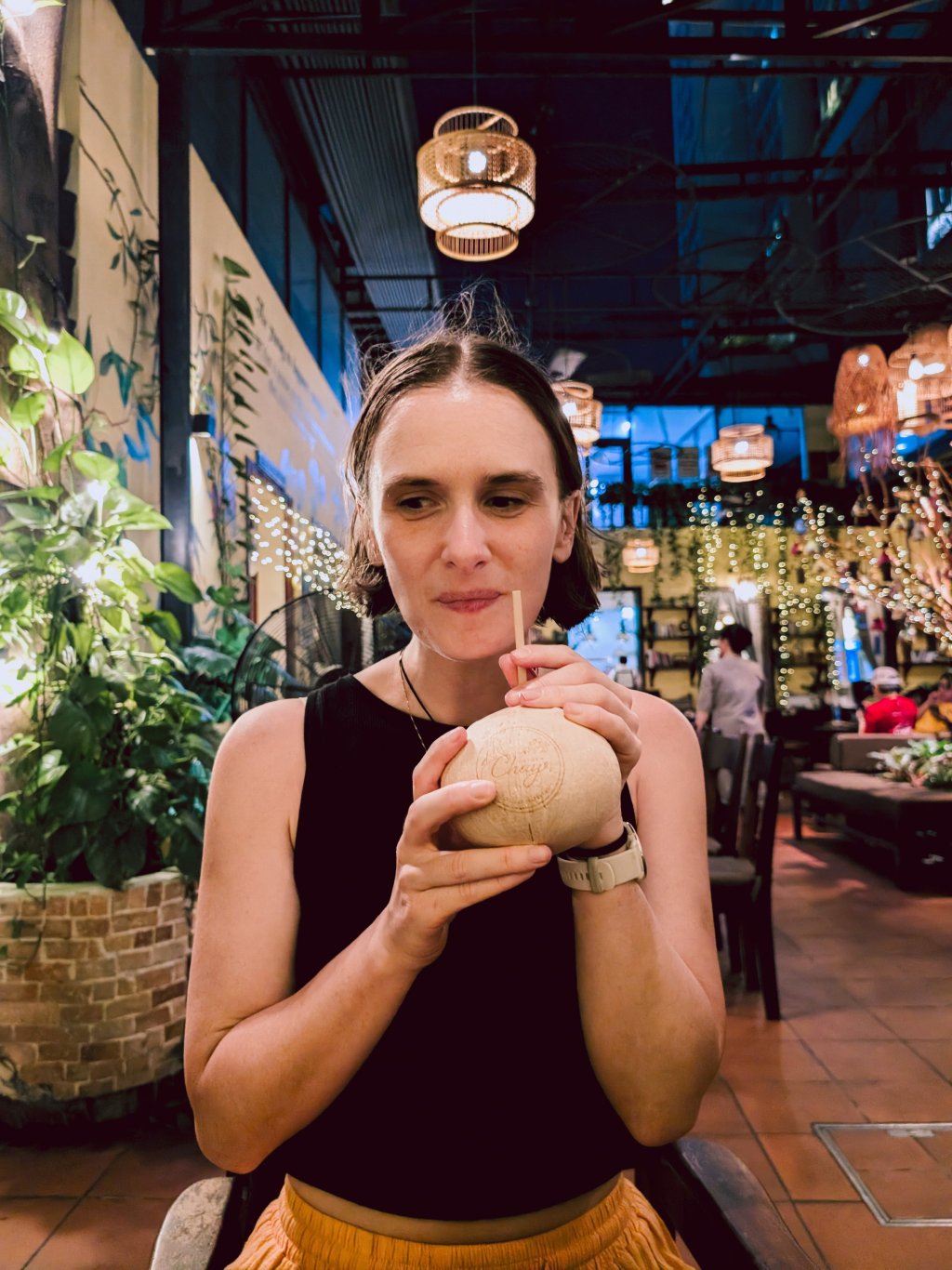 Woman holding a coconut drink in a warmly lit restaurant in Ho Chi Minh City.