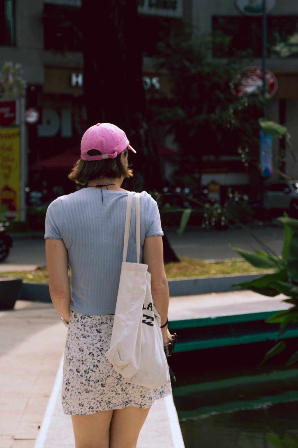 Person wearing a pink hat and carrying a white bag walking along a city waterfront.