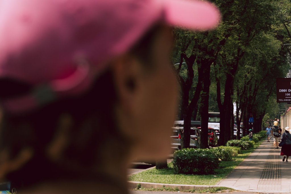 Person wearing a pink hat walking along a tree-lined street in Ho Chi Minh City.