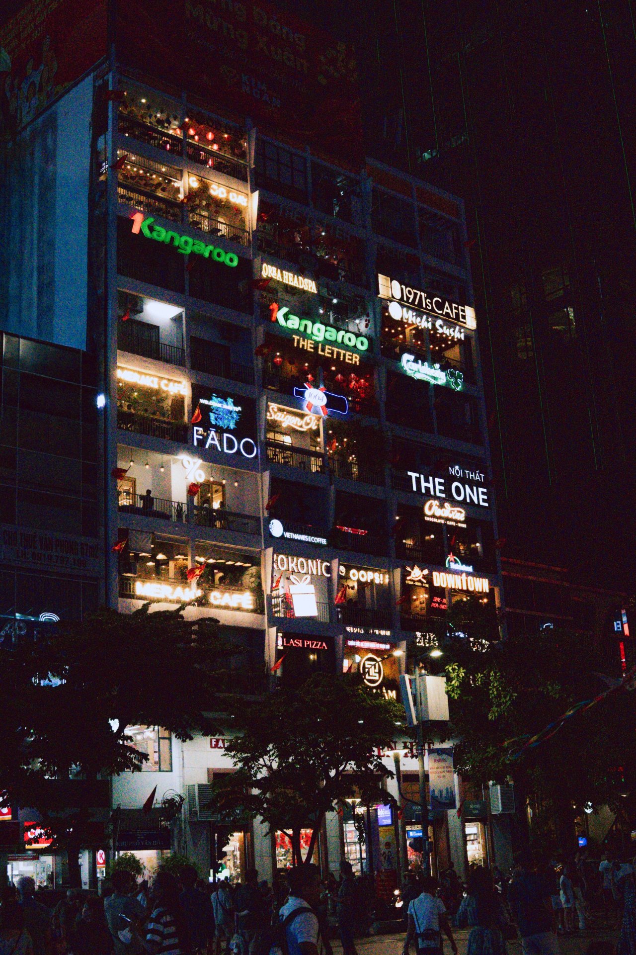 Nighttime street view of illuminated commercial buildings and vibrant city lights in Ho Chi Minh City.