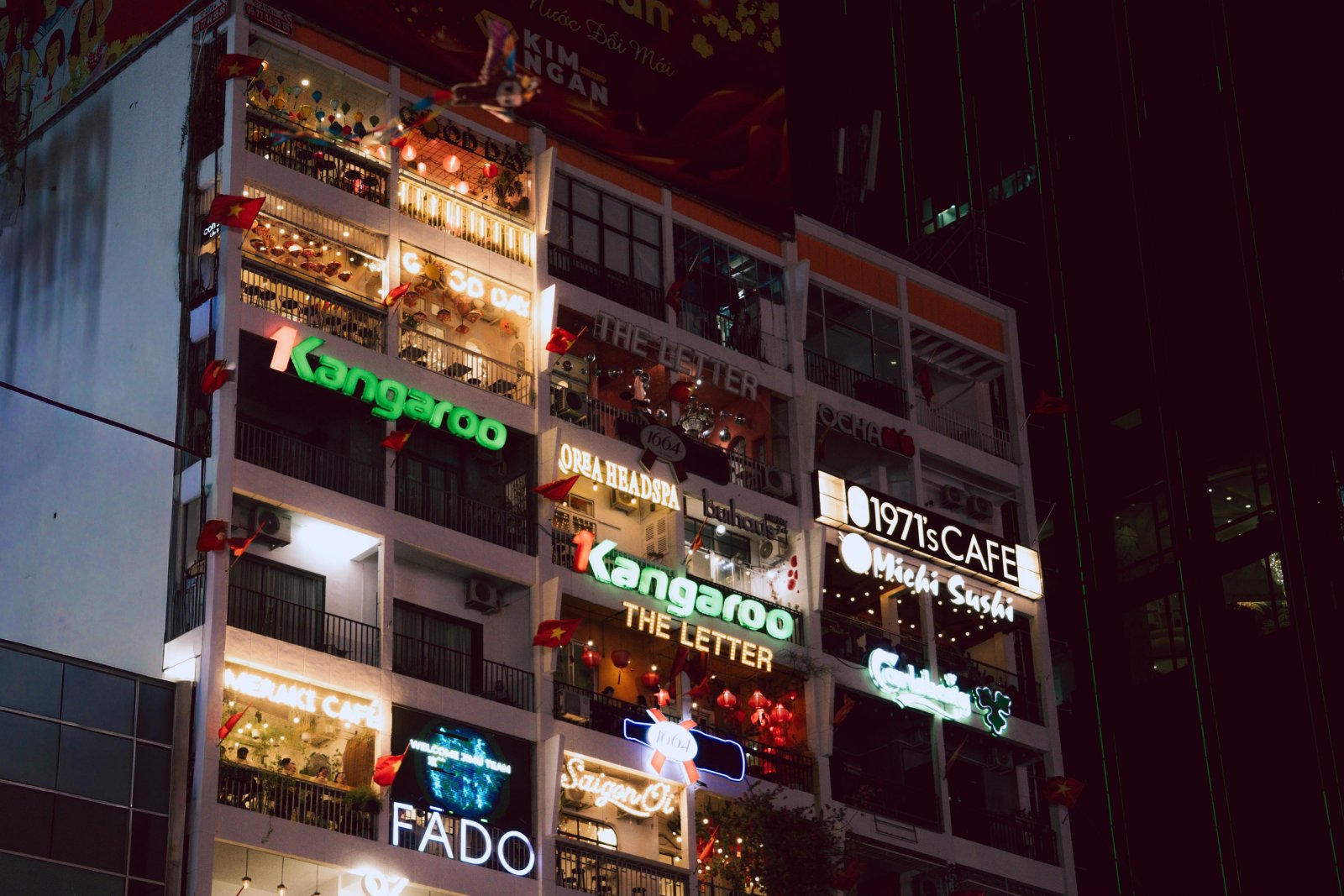 Nighttime street view of vibrant commercial buildings and illuminated storefronts in Ho Chi Minh City.