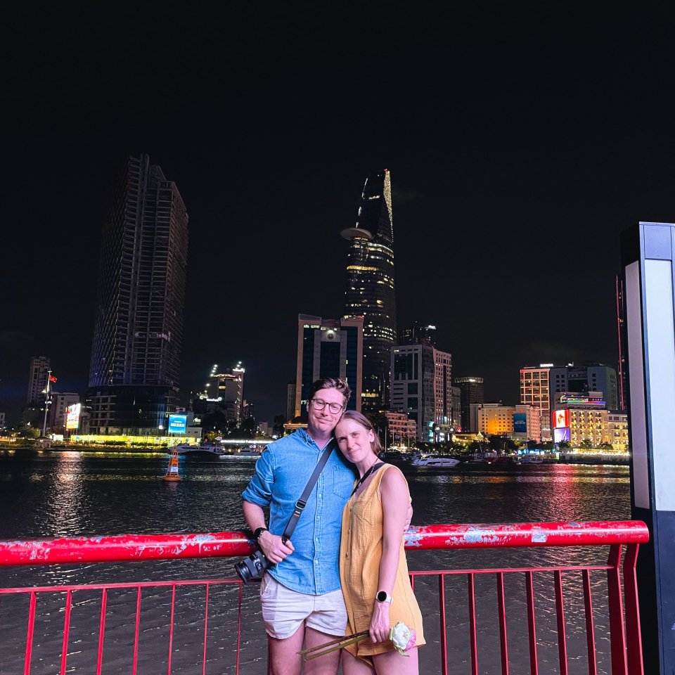 Two people standing by a railing overlooking a city skyline at night.