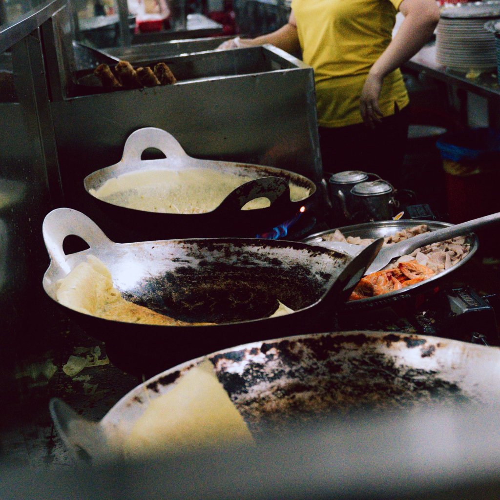 Person cooking in a busy kitchen with frying pans.