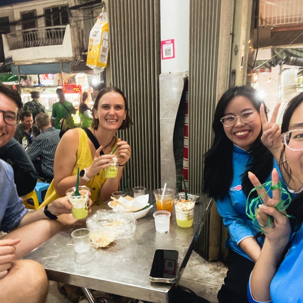 Group of people smiling while sitting at a table with drinks in a street setting.