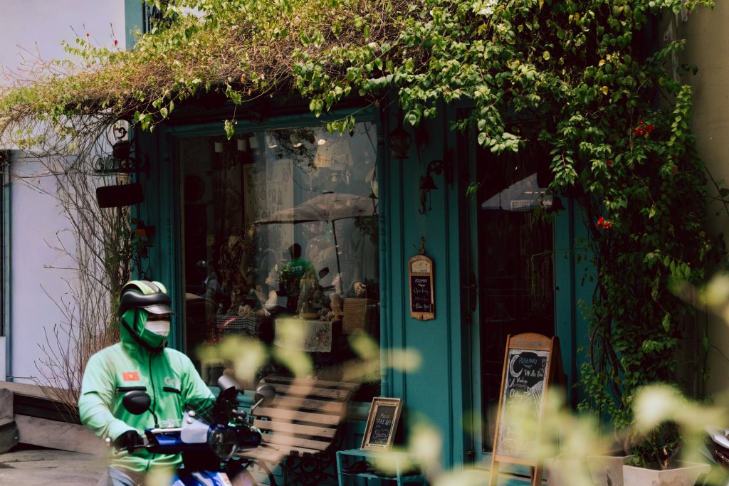 Person on a scooter in front of a storefront with greenery in Ho Chi Minh City.