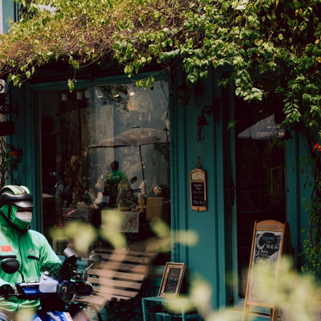 Person on a scooter in front of a storefront with greenery in Ho Chi Minh City.