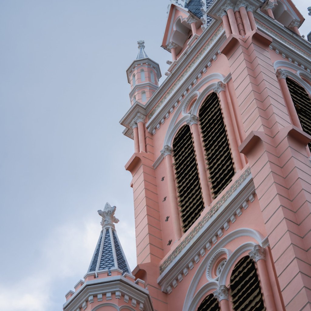 Architectural detail of a pink and white building facade with pointed roofs.