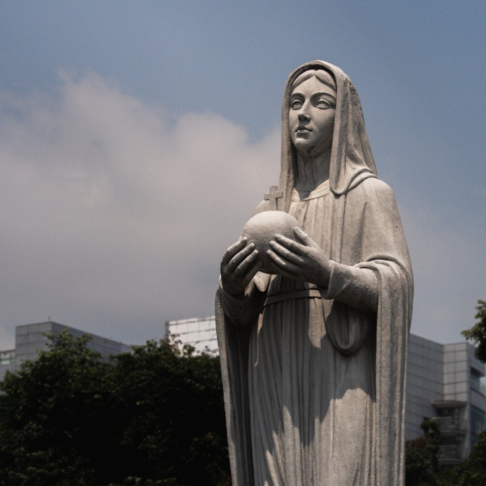 Stone statue of a woman holding a globe in front of a city skyline.