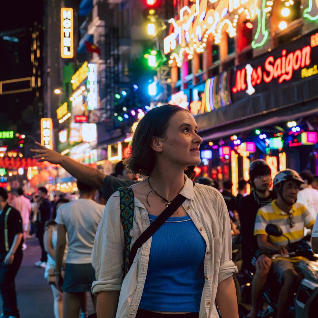 Woman walking on a busy street at night with bright neon lights in the background.