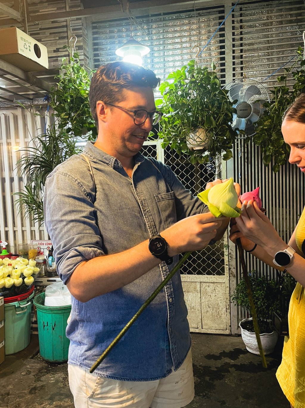 Two people examining and holding yellow flowers in a market setting.