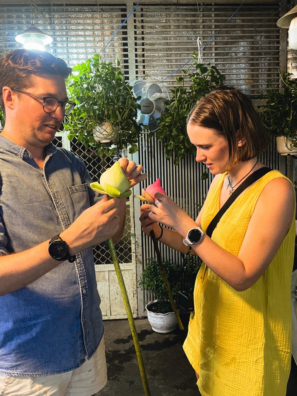 Two people examining light green flowers in a setting with hanging plants.