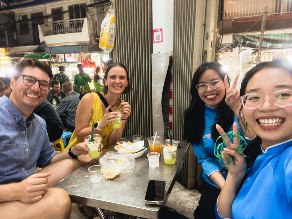 Group of people smiling while enjoying food and drinks at a street food stall.