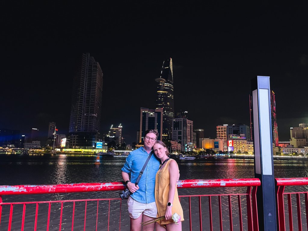 Two people standing on a bridge overlooking a city skyline at night.
