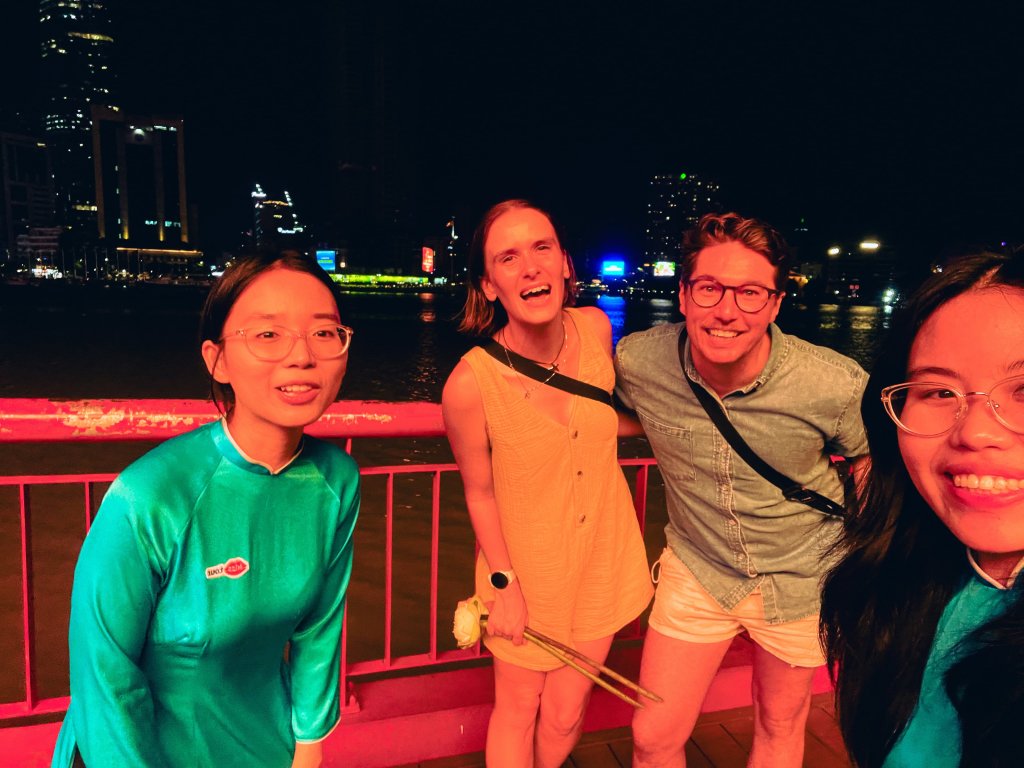 Group of people posing outdoors near a body of water at night.