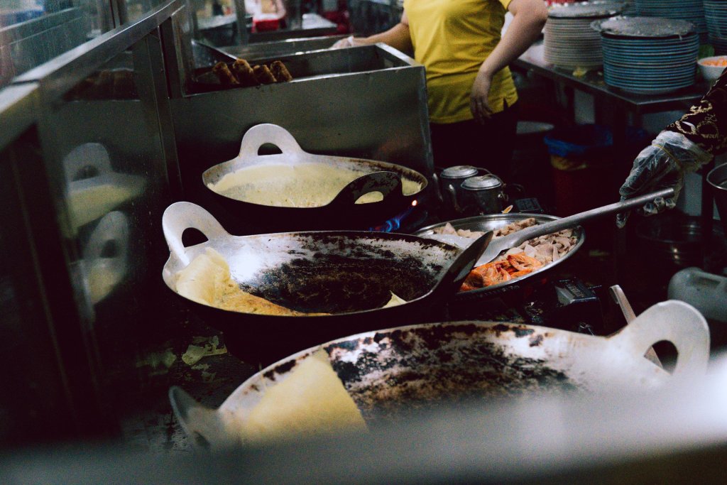 Hands in a kitchen stirring food in frying pans.
