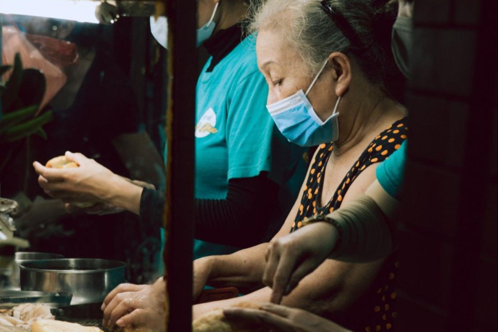 A masked vendor prepares b&aacute;nh m&igrave; at a small Hội An street stall.