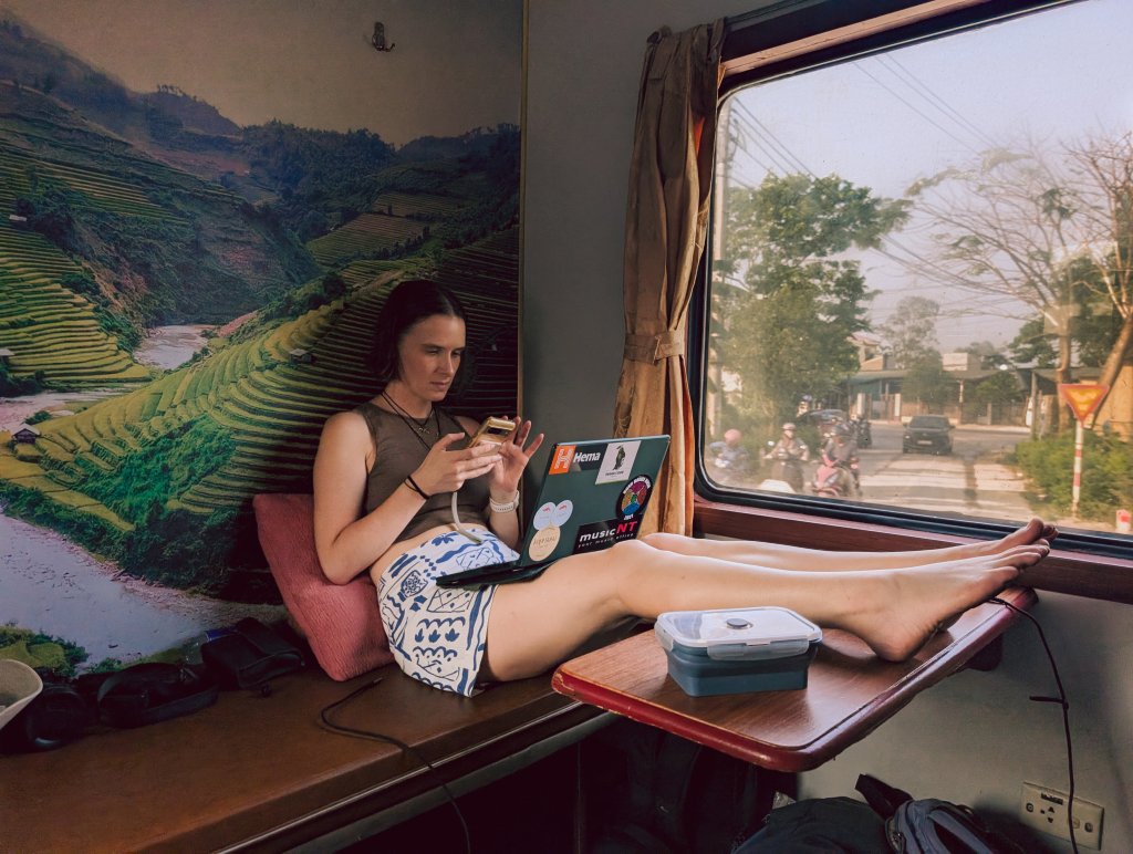 A traveller sitting in a private train cabin in Vietnam with rice fields visible through the window.