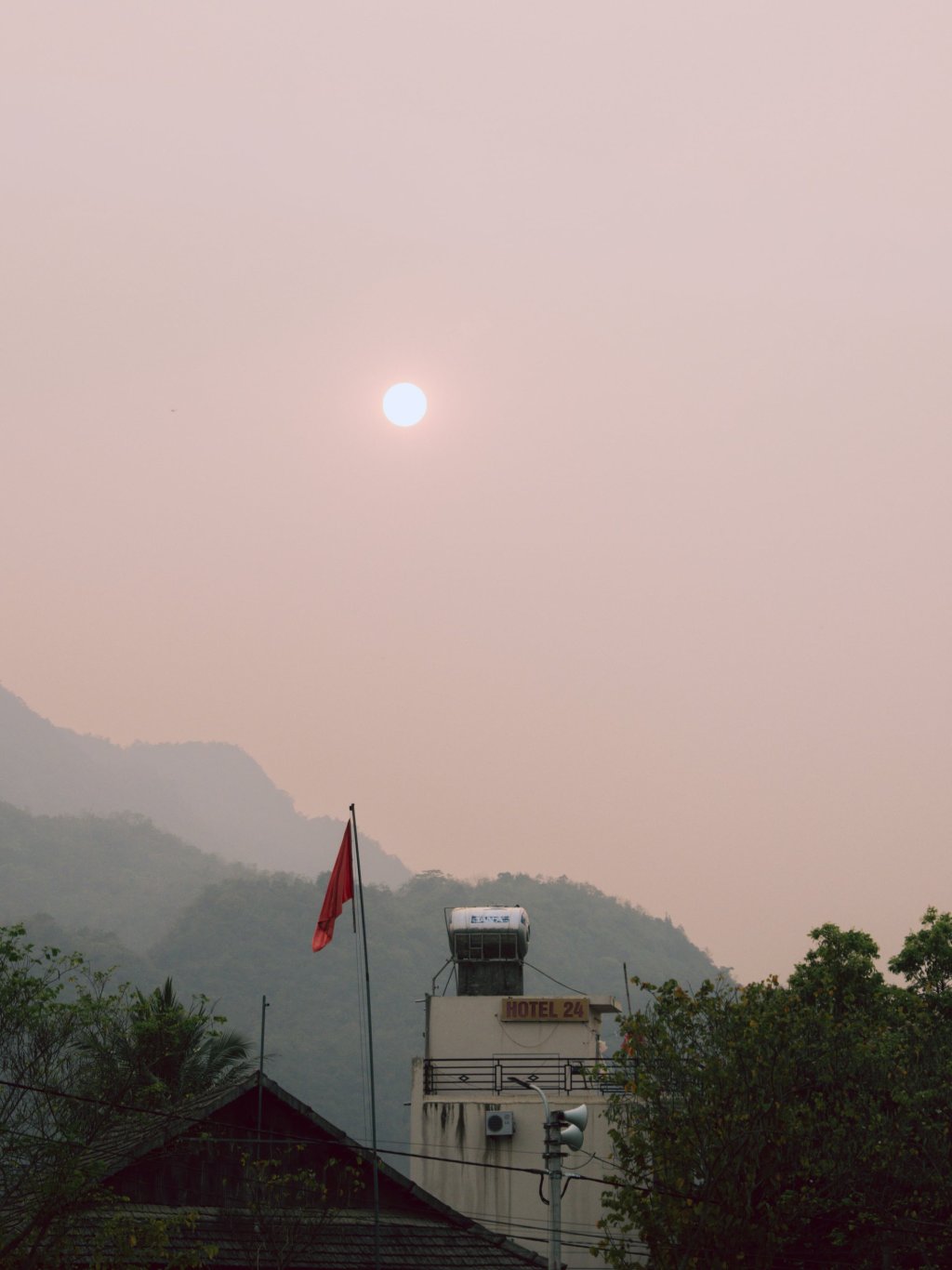 View of a building and a red flag against a hazy background with a bright sun.
