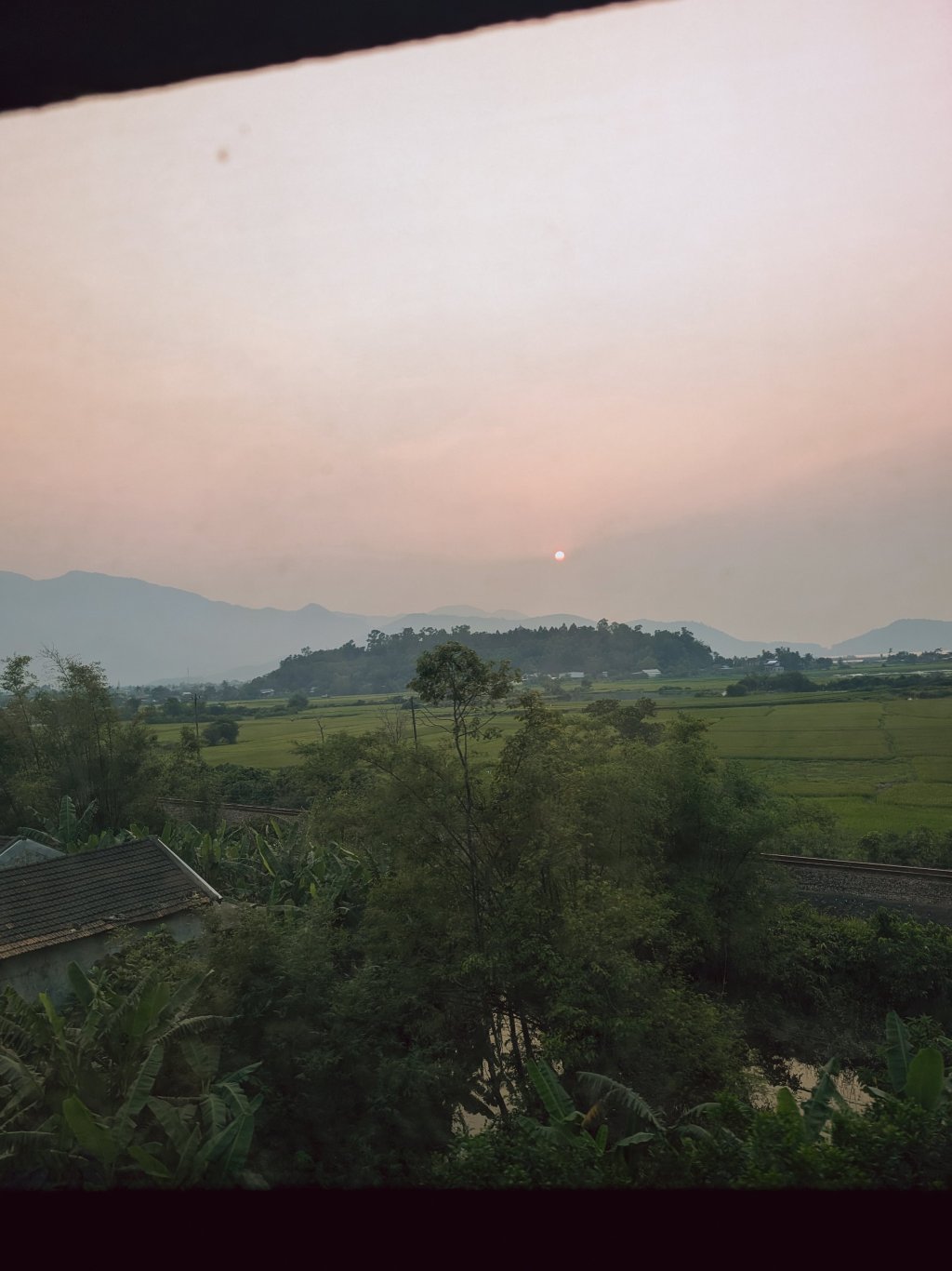 Hazy landscape with fields and distant hills under a soft light.