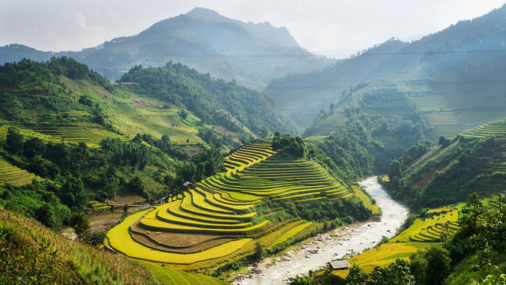 Rolling green hills of terraced fields along a river in a mountainous landscape.
