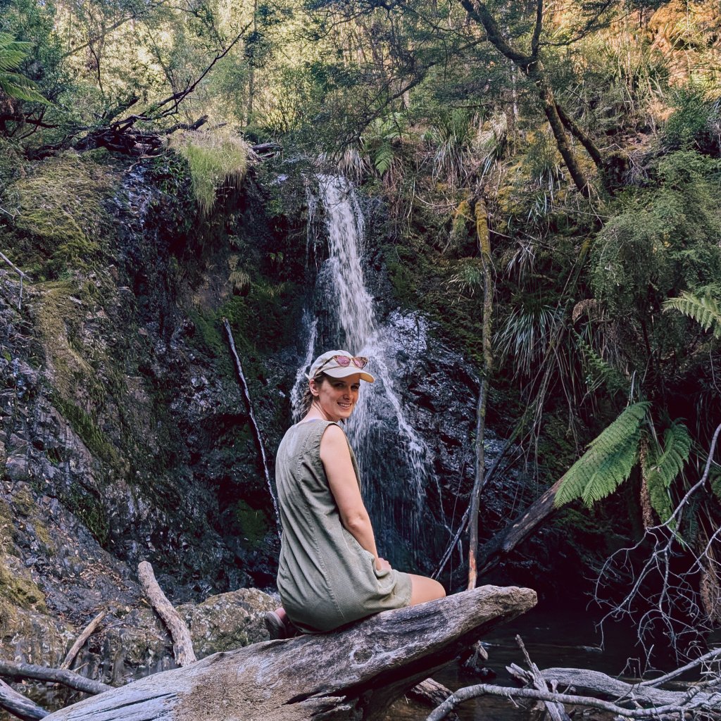 Hannah sitting on a fallen log in front of a waterfall