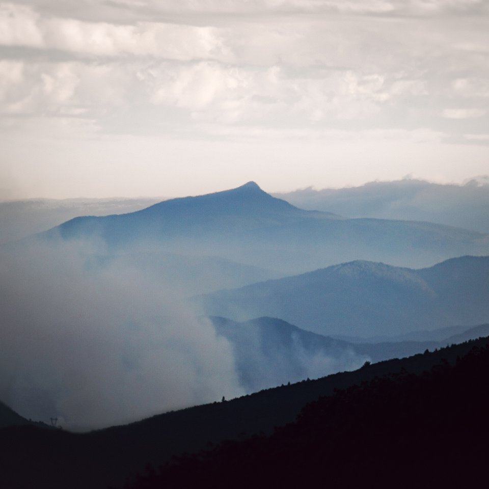 Layered blue mountain ridges fading into a misty horizon under a soft, cloudy sky.