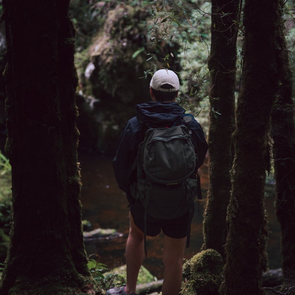 Chris standing between moss-covered trees while looking out at a dark forest pool.