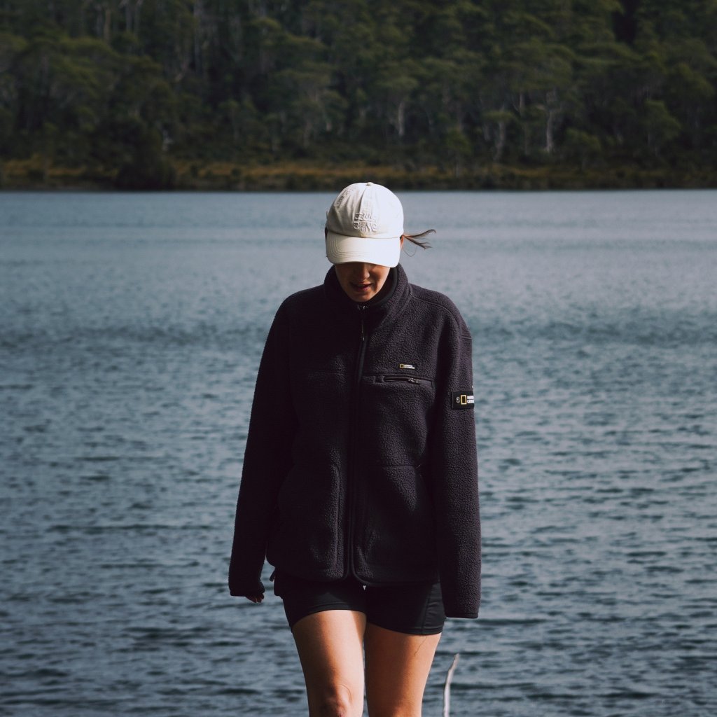 Hannah walking along the edge of a calm lake with a dense green forest in the background.