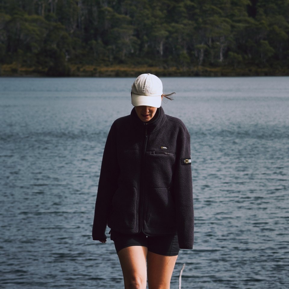 Hannah walking along the shoreline of a calm lake with a dense green forest in the background.