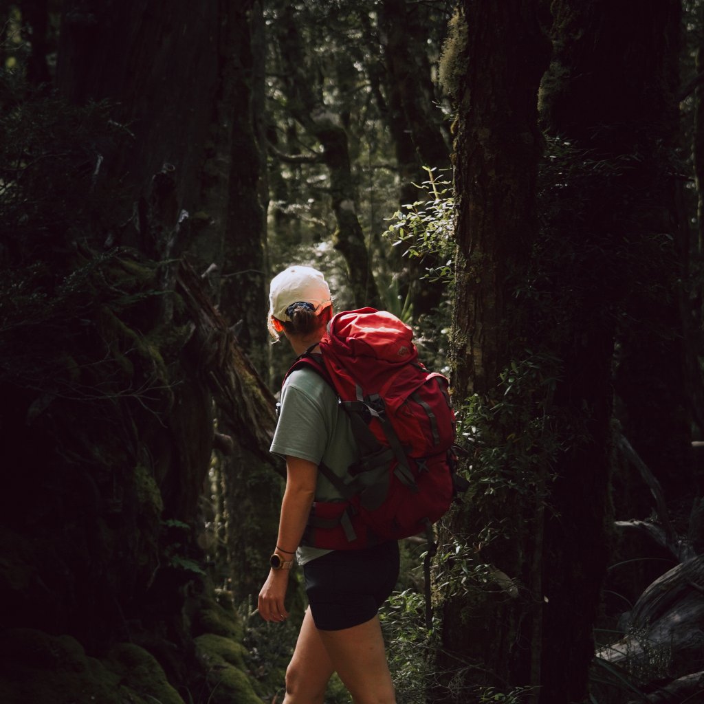 Hannah wearing a red backpack while hiking through a dense, mossy forest in Tasmania.