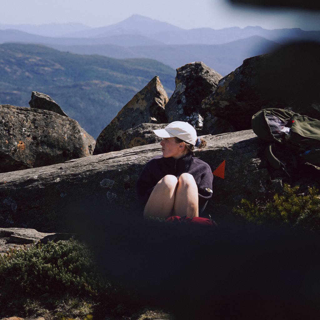Hannah resting on a rocky outcrop, looking out over the layered blue mountain ranges of Tasmania.