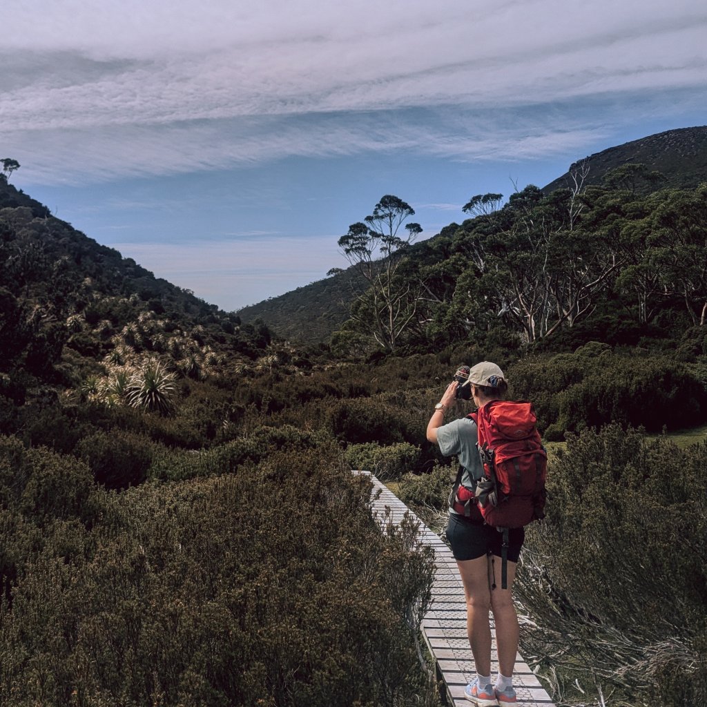 Hannah with a red backpack taking a photo from a boardwalk in the Tasmanian wilderness.