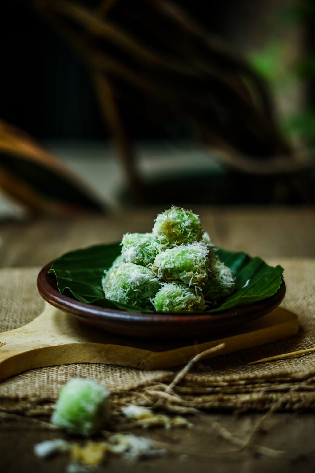 Green klepon rice cakes covered in grated coconut on a dark plate.