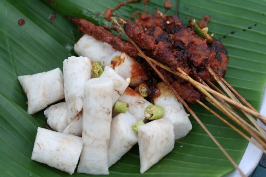 Sate bulayak skewers served with spiral-wrapped rice cakes on a banana leaf.