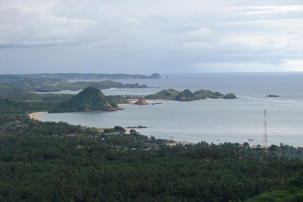 View of a coastline with small islands and a transmission tower under a cloudy sky.