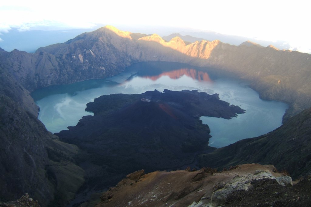 View of a mountain lake reflecting in the surrounding peaks during sunrise.